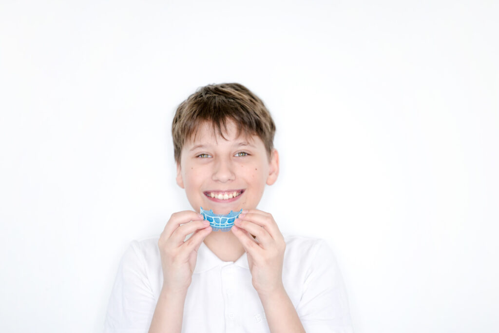 Teen boy put mouthguards on his mouth on white background. Blue mouthguards made of silicone or thermoplastic material.
