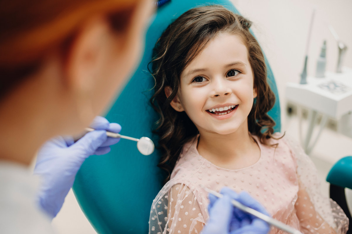 Lovely little kid smiling while talking with the pediatric dentist after doing a tenth examination in a pediatric stomatology.