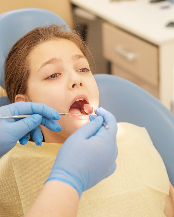 The hands of an unrecognizable pediatric dentist conducting an examination procedure for a smiling cute little girl sitting on an armchair in the office. Dentist's office. A little girl sitting at the dentist.