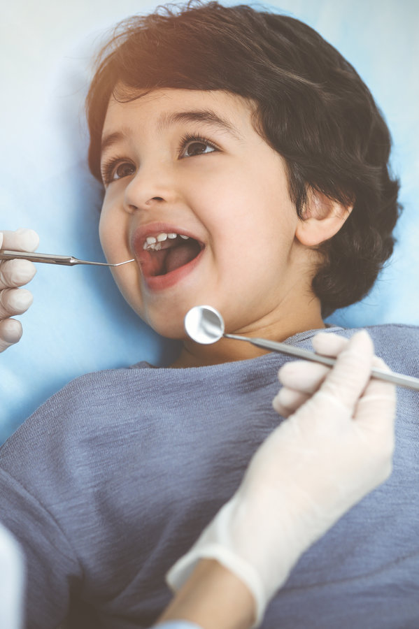 Cute arab boy sitting at dental chair with open mouth during oral checking up with doctor. Visiting sunny dentist office.