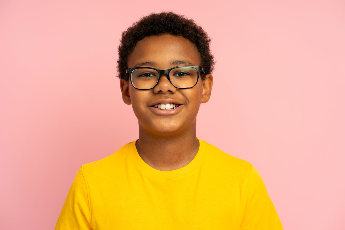 Portrait of smiling school boy wearing stylish eyeglasses looking at camera isolated on pink background. Education concept