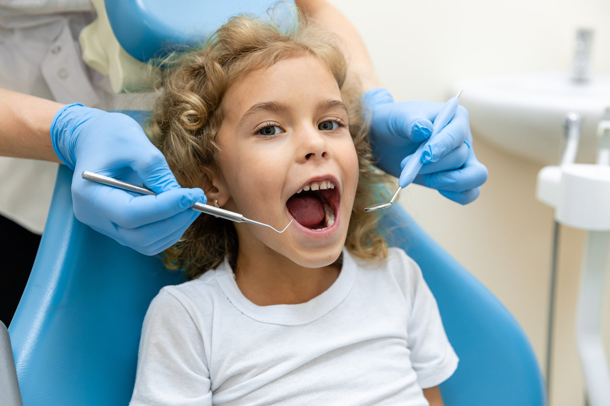 dentist, doctor examines the oral cavity of a little girl, uses a mouth mirror, baby teeth close-up, the concept of pediatric dentistry, dental treatment.