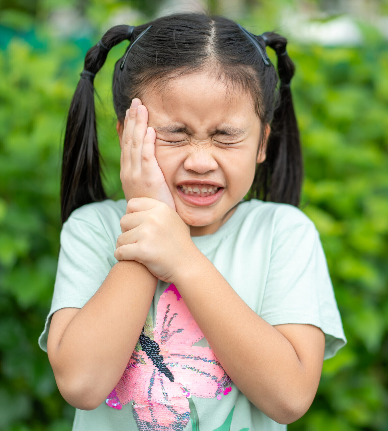 Tooth ache concept. Asian Little girl holding her cheek with hand, suffering from bad toothache. Kid with painful expression .Caries. a loose tooth, Severe tooth pain.