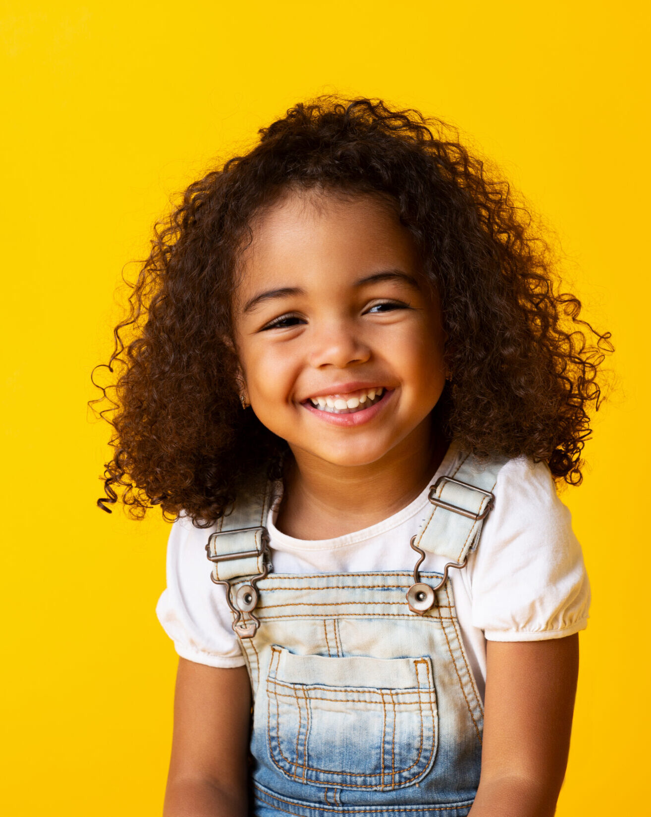 Happy african-american child girl smiling to camera over yellow background