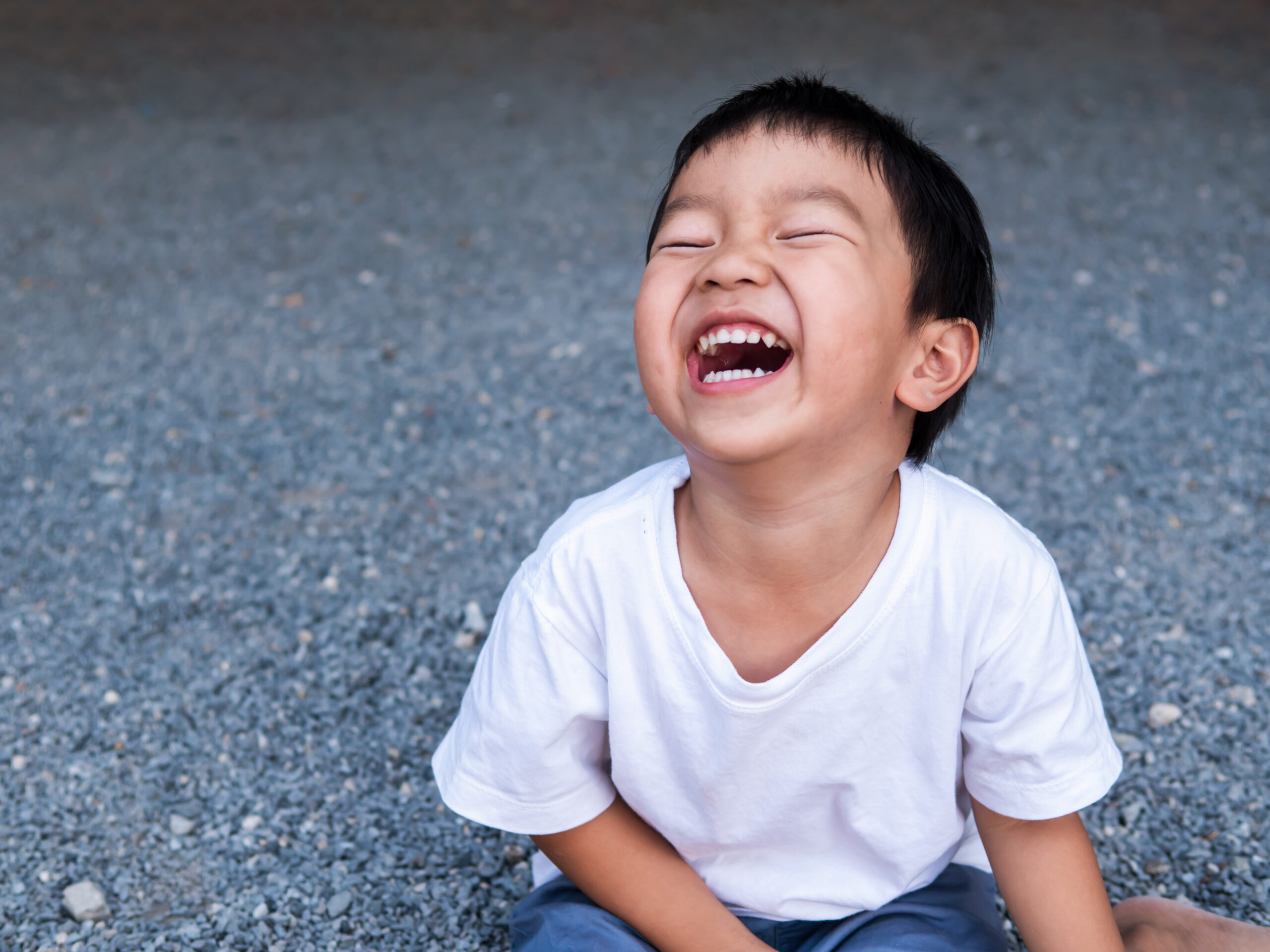 Asian cute little child boy laughing with mouth open wide, seeing whitening teeth. Happy Kid in white shirt enjoy in funny shot in relaxing day.