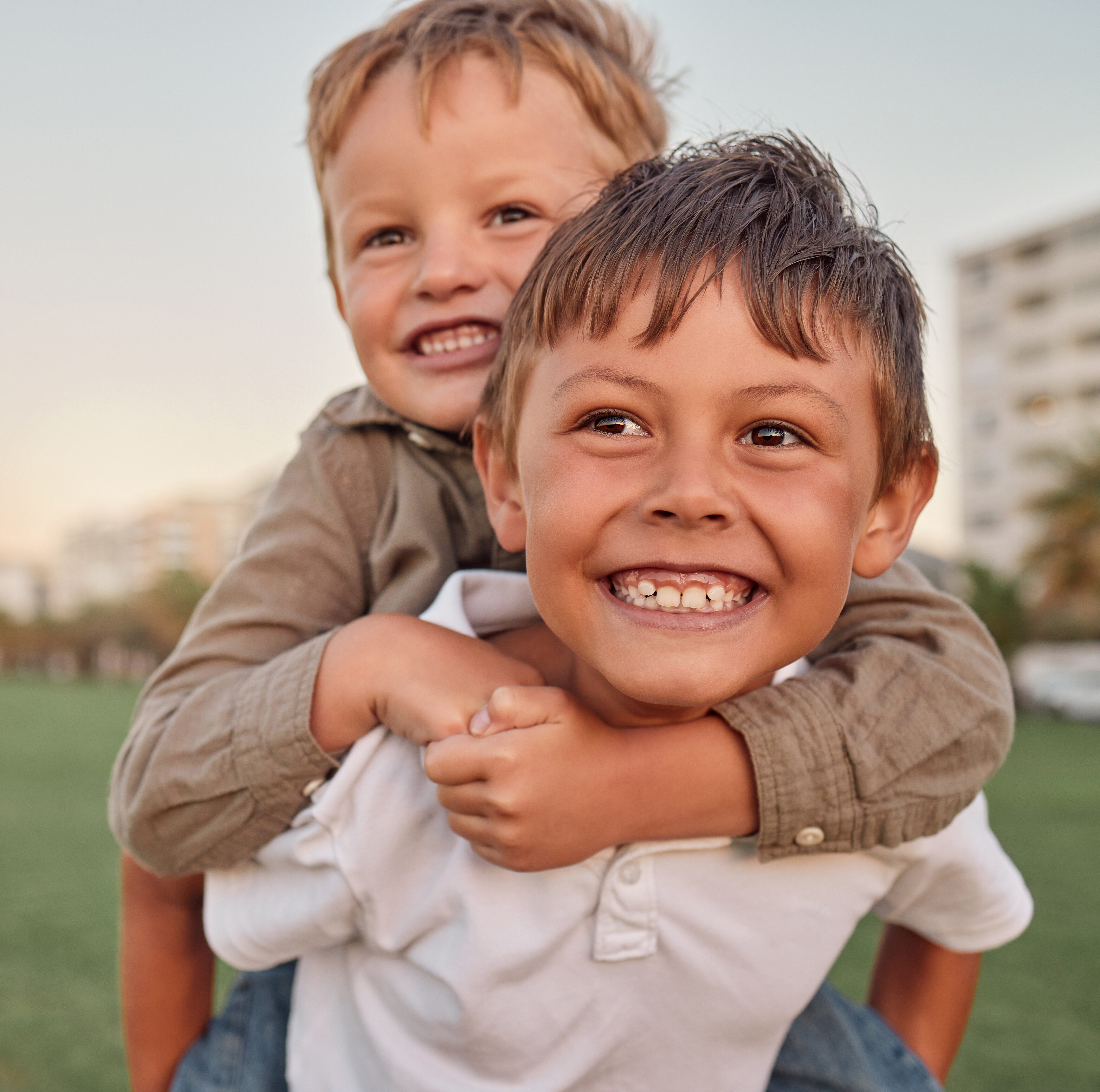 Happy, smile and portrait of brothers with piggyback ride playing in a park together on vacation. Happiness, excited and children bonding in nature while on a summer holiday adventure in Australia
