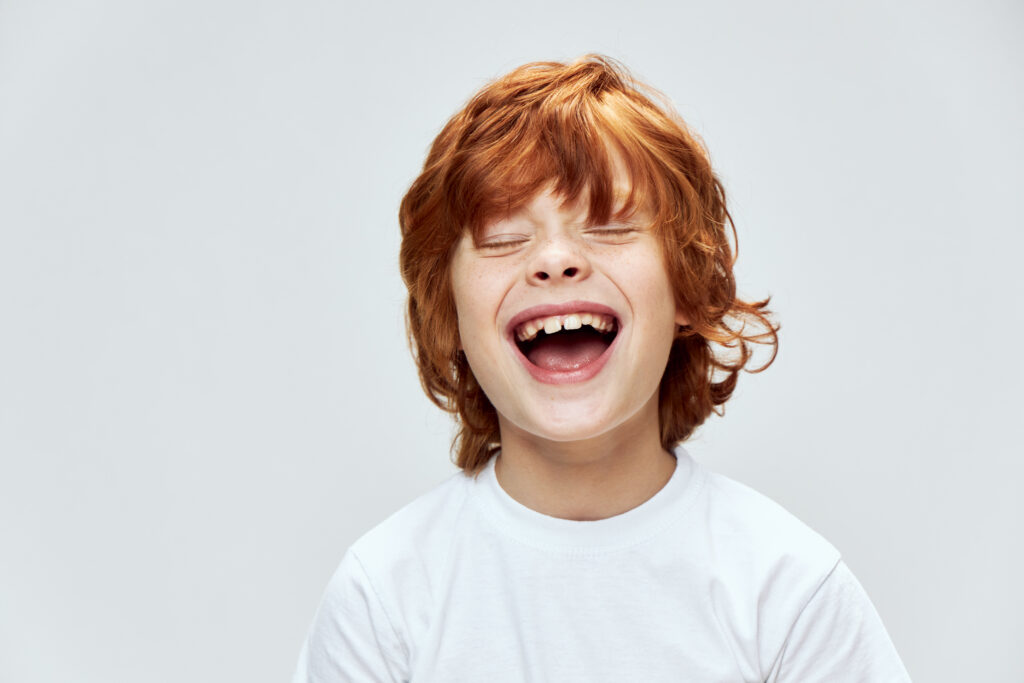 funny red-haired boy with closed eyes with wide open mouth smile cropped view of white t-shirt