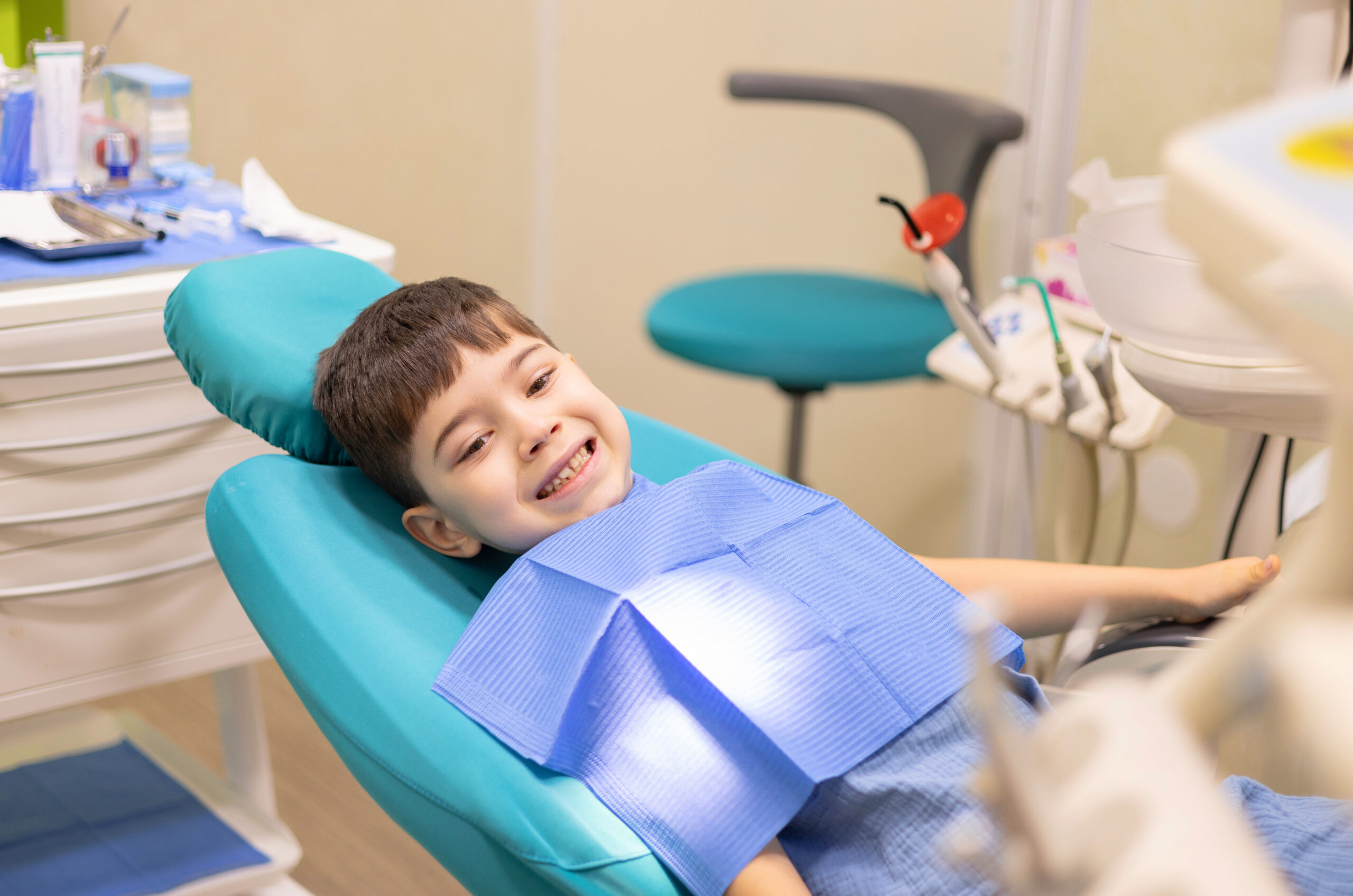 kid in dental office. dentist checking child teeth using tools mouth mirror and scalar.crying with tears, sad boy is afraid.doctor looking at screen,tooth filling treatment.kid in chair being examined